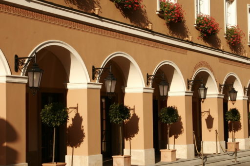 Fasada budynku z arkadami w stylu klasycystycznym, wyposażona w kinkiety 21 Leda montowane na ozdobnych, kutych wspornikach. Oprawy oświetleniowe podkreślają elegancki charakter obiektu i harmonizują z detalami architektonicznymi.