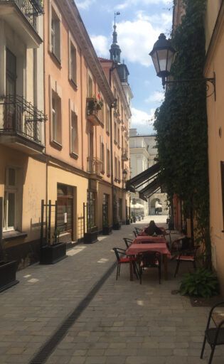 Ulica w centrum Kalisza z oprawą oświetleniową 01D Vera zamontowana na wysięgniku naściennym. Oprawa wkomponowana w historyczną zabudowę, stanowi element miejskiego oświetlenia w strefie pieszej.